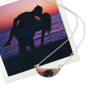 A customizable crescent shaped necklace featuring a photo of a couple on the beach